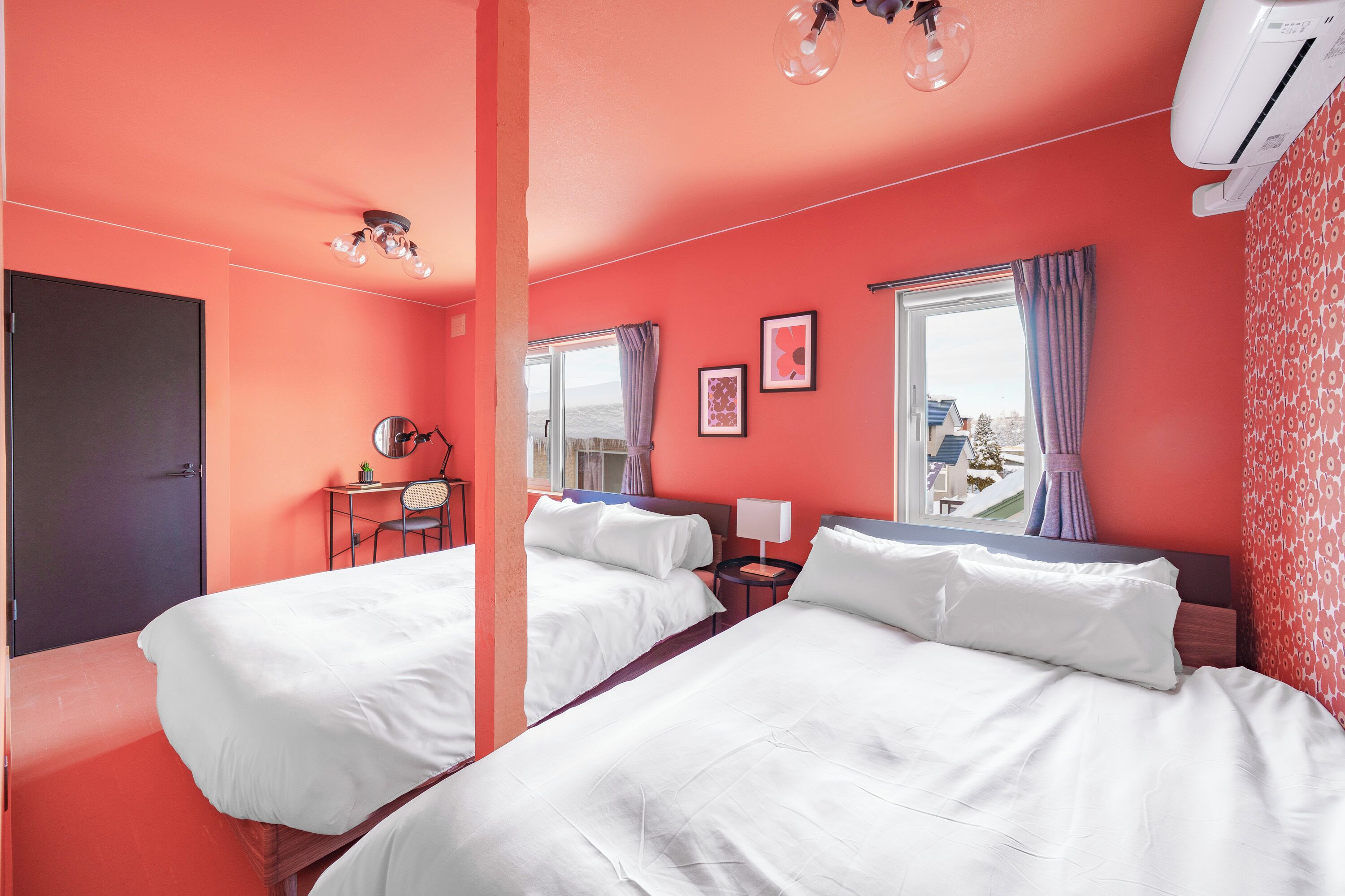 A hotel room with two beds, a desk, a chair, and a window with curtains.