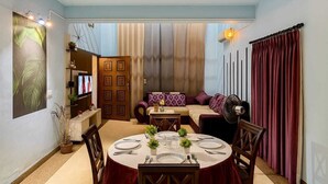 Un comedor con una mesa redonda preparada para cuatro personas, un sofá y un televisor al fondo.