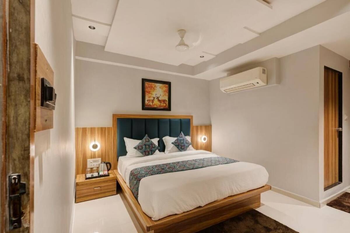 A modern bedroom with a wooden bed frame, a headboard with built-in lighting, a bedside table with a lamp, and an air conditioning unit on the wall.