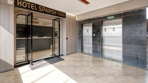 Ένας χώρος υποδοχής ξενοδοχείου με γραφείο υποδοχής, μια είσοδο με γυάλινη πόρτα και έναν ανελκυστήρα για χρήση σε περίπτωση πυρκαγιάς.
