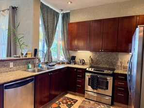 A kitchen with wooden cabinets, a stainless steel refrigerator, a built-in oven, and a granite countertop. - Beachfront West Bay 2BR Condo: Reef Snorkel Paradise! (Coxen Hole)