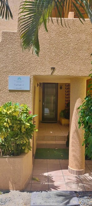 A building entrance with a textured wall, a sign indicating 'Oceanfront Dream Coral Suites #17,' and a door leading inside.