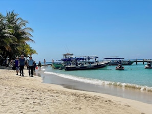 A beach with boats, palm trees, and people walking along the shore.