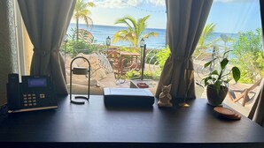 Une pièce avec un bureau, un ordinateur portable, une petite plante, une figurine de chat et une vue sur l’océan.