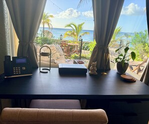 Una habitación con escritorio, una computadora portátil, una planta pequeña, una figura de gato y vistas al océano.