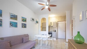 A living room with a sofa, a dining table with chairs, a kitchen area, and a ceiling fan.