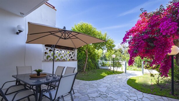 An outdoor patio with a table and chairs, a beige umbrella, and a stone floor.