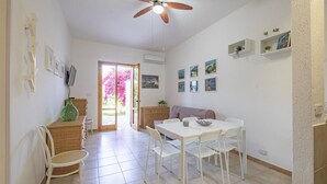 A dining area with a table and chairs, a ceiling fan, and a door leading to a garden with pink flowers.