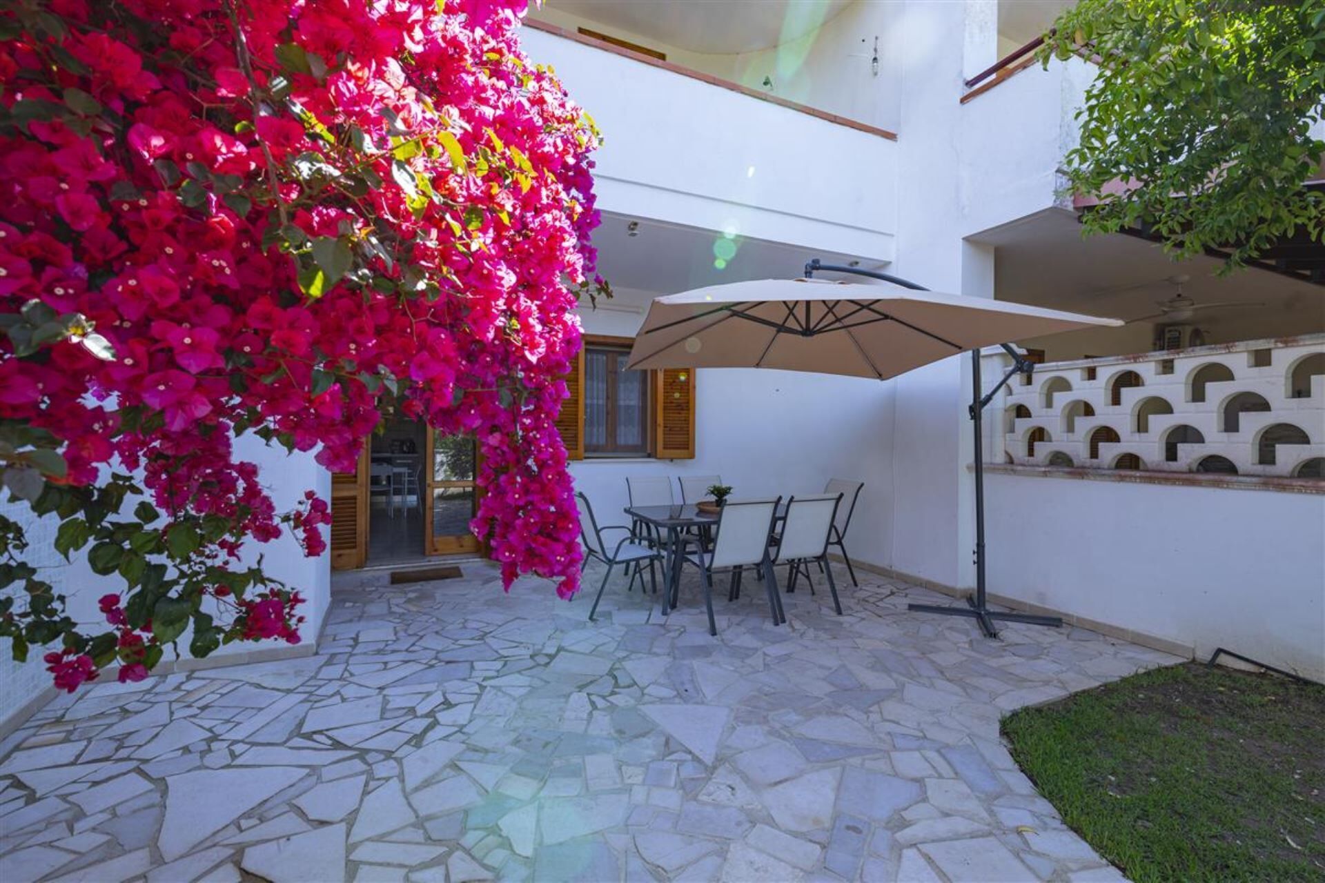 An outdoor patio with a stone floor, a table with chairs, and a large umbrella.