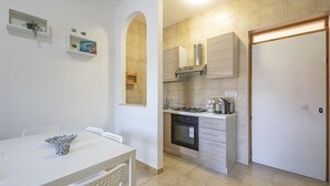 A compact kitchen with a stove, oven, and cabinets, a dining area with a table and chairs, and a door leading to another room.