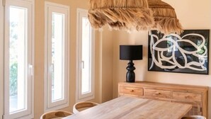Ein Essbereich mit einem Holztisch, zwei hängenden Rattan-Kronleuchtern, einer schwarzen Lampe und einem an der Wand befestigten abstrakten Kunstwerk.