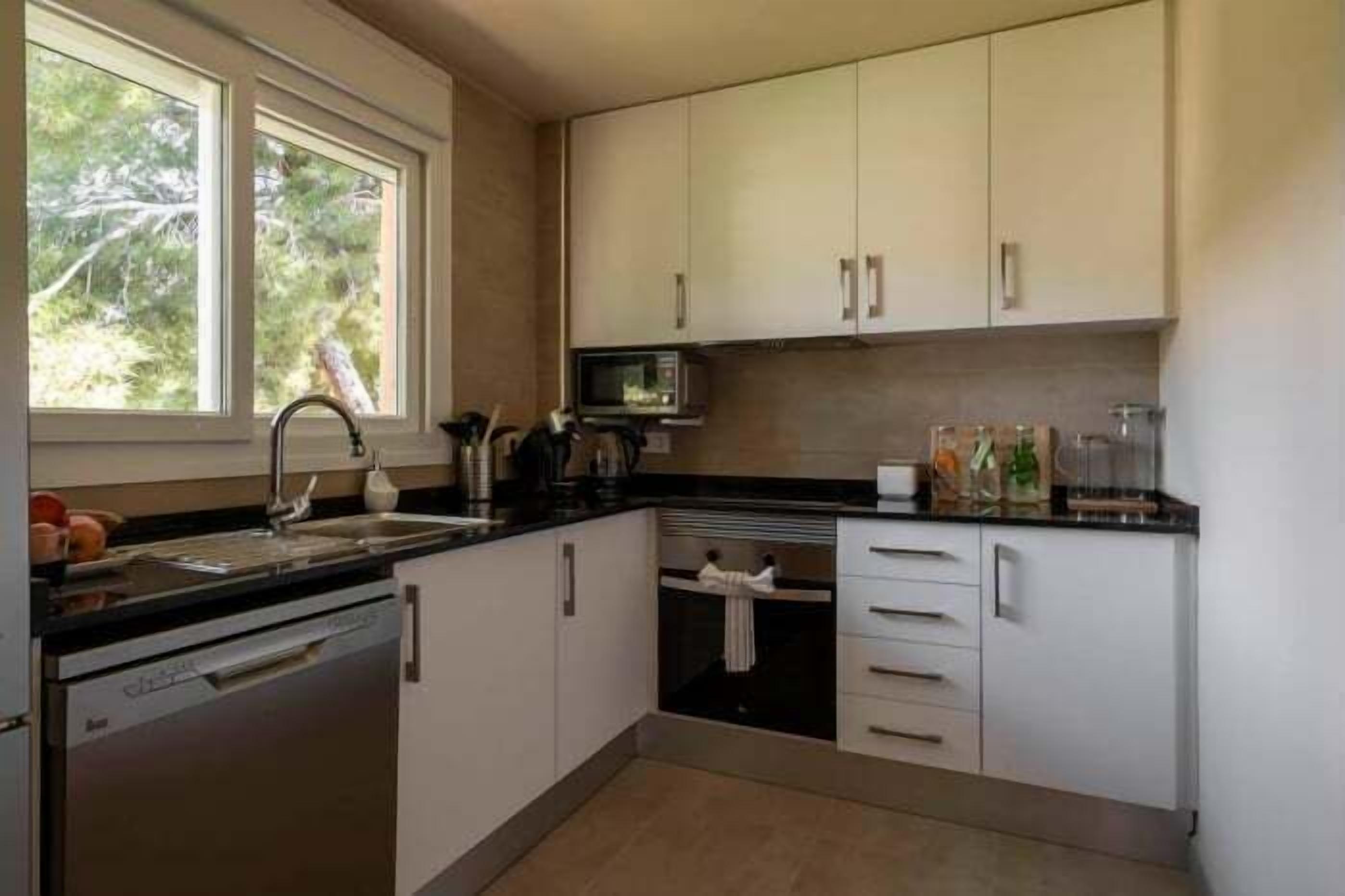 A modern kitchen with white cabinets, a black countertop, a built-in microwave, and a dishwasher.