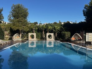 A swimming pool with three circular architectural features, surrounded by trees and buildings. - Luxury Apartment in Moraira – Ritual de Terra (Teulada)