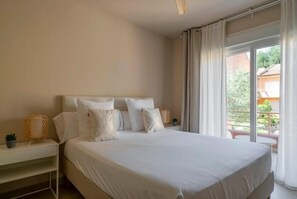 A bedroom with a large bed, a bedside table with a lamp, and a view of the outdoors through a balcony. - Luxury Apartment in Moraira – Ritual de Terra (Teulada)