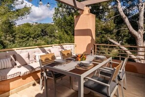 An outdoor dining area with a table set for two, a cushioned seating area, and a pergola with string lights. - Luxury Apartment in Moraira – Ritual de Terra (Teulada)