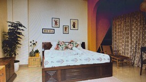 Een slaapkamer met een houten bed, een grote kamerplant, een nachtkastje en een stoel.