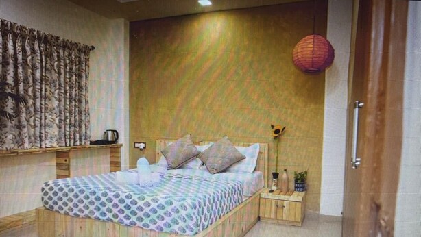 Een slaapkamer met een bed, kussens, een nachtkastje, een lamp en een wandplank.