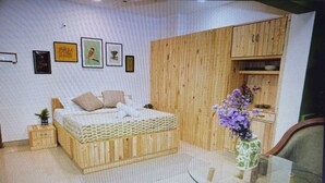 Een slaapkamer met een houten bed, een klein nachtkastje, een glazen tafel met een bloemenvaas, en een houten kledingkast.