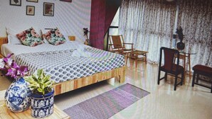 Een slaapkamer met een bed, stoelen, een tafel en een raam met gordijnen.