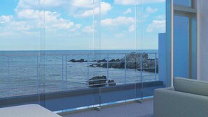 A balcony with a view of the sea and rocks, a glass door, and a sofa.