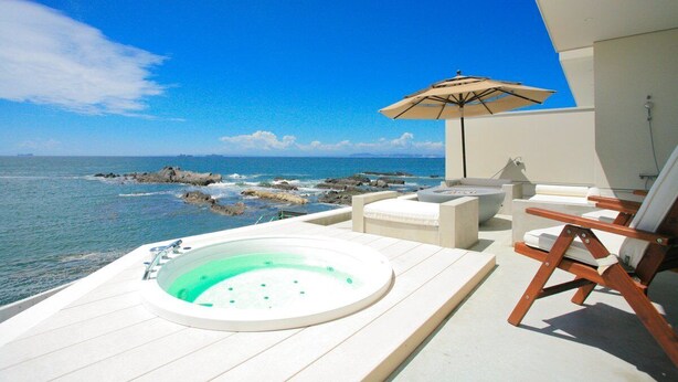 A balcony with a hot tub, lounge chairs, and an umbrella overlooking the ocean.