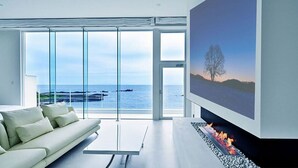 A modern living room with a sofa, a fireplace, and a large window overlooking the sea.
