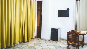 A room with yellow curtains, a wooden chair, a small black cabinet, and a television mounted on the wall. - Roomshala Hotel Iconic Near Karol Bagh (New Delhi)