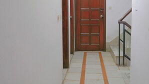 A narrow hallway with a wooden door at the end, white walls, and a tiled floor with orange stripes. - Roomshala Hotel Iconic Near Karol Bagh (New Delhi)