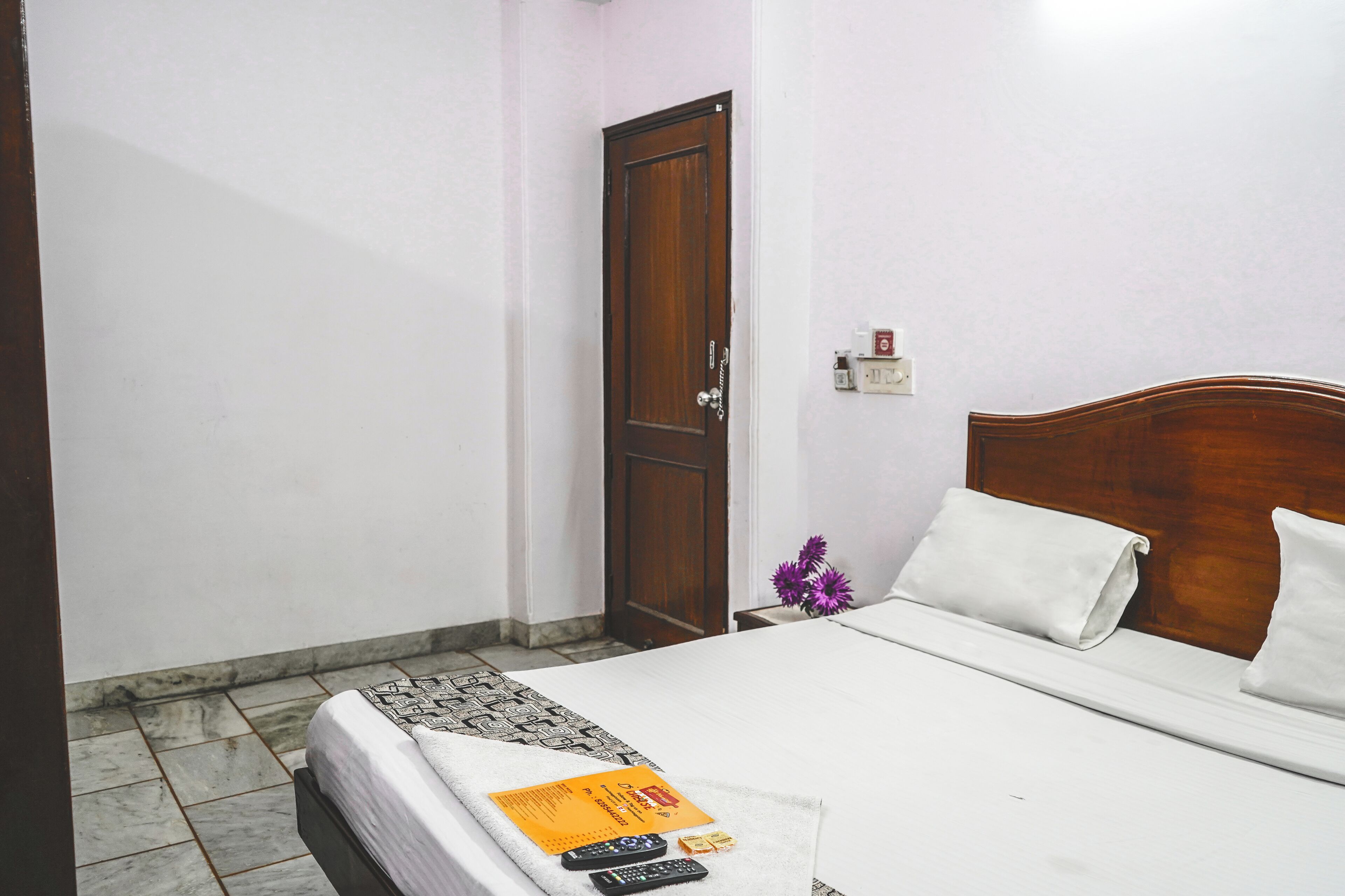 A neatly made bed with white linens, a wooden headboard, and a small nightstand with a vase of flowers.
