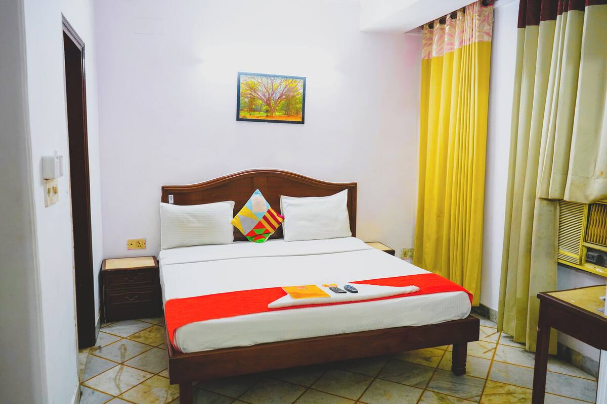 A neatly made bed with a red blanket, a wooden headboard, and a pillow with a geometric pattern.