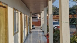 Un pasillo cubierto con suelo de baldosas, puertas de madera y vista a vehículos estacionados y follaje al fondo.