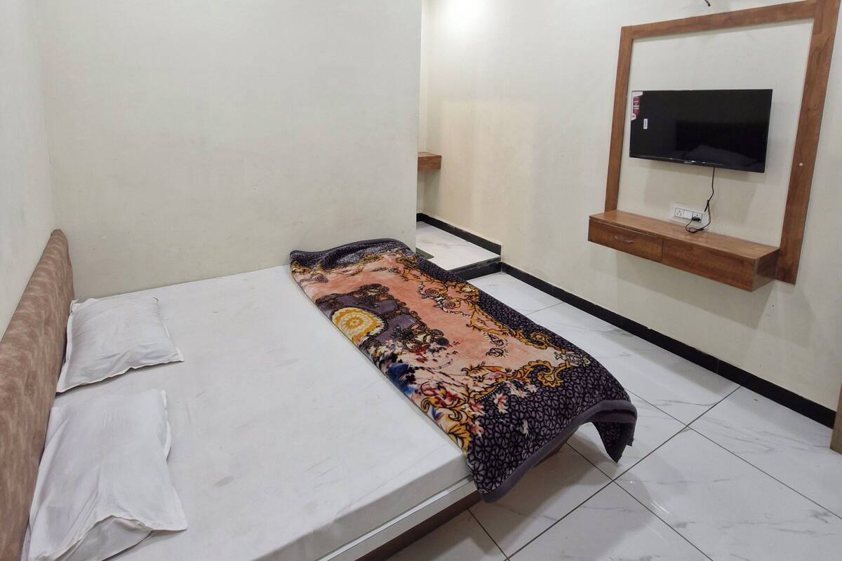 Un dormitorio con una cama, un ventilador de techo, un televisor montado en la pared y una alfombra estampada.