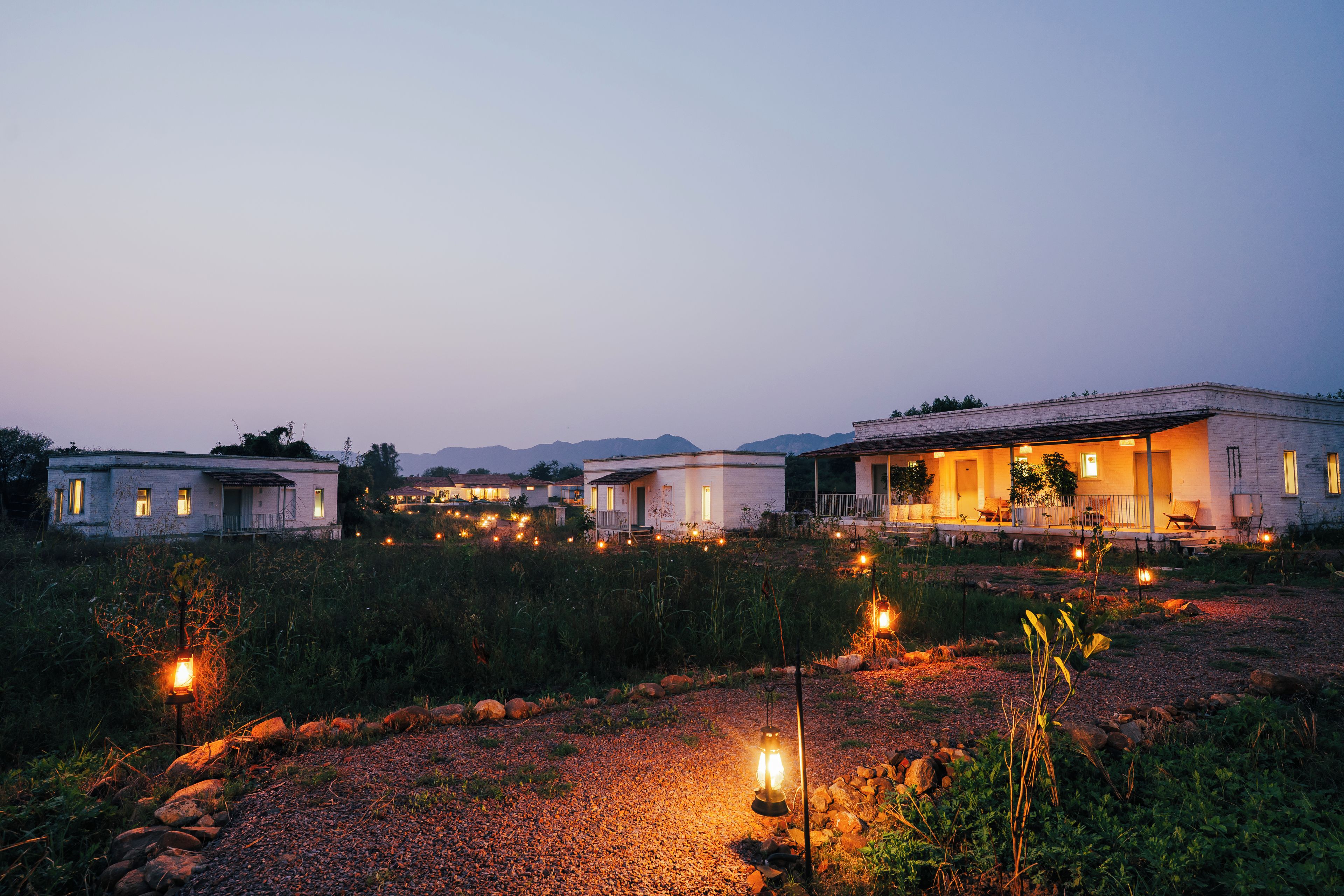A row of white buildings with outdoor lighting, surrounded by a natural landscape.