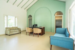 A spacious room with a green brick wall, a wooden desk with a computer, a floral sofa, and a blue armchair. - Kadamb Bagh (Rajgarh)