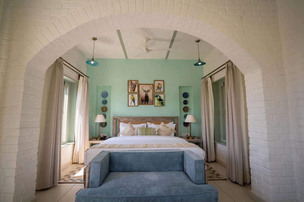 A bedroom with a bed, a blue armchair, a ceiling fan, and a brick wall arch.