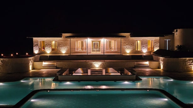Un edificio moderno con piscina antistante, caratterizzato da facciata in pietra e finestre illuminate.