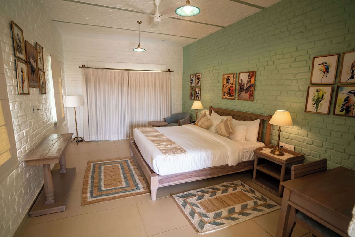 A bedroom with a bed, bedside tables, a desk, a chair, a window with curtains, and artwork on the walls.