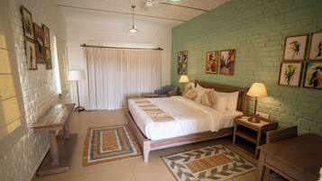 A bedroom with a bed, bedside tables, a desk, a chair, a window with curtains, and artwork on the walls.
