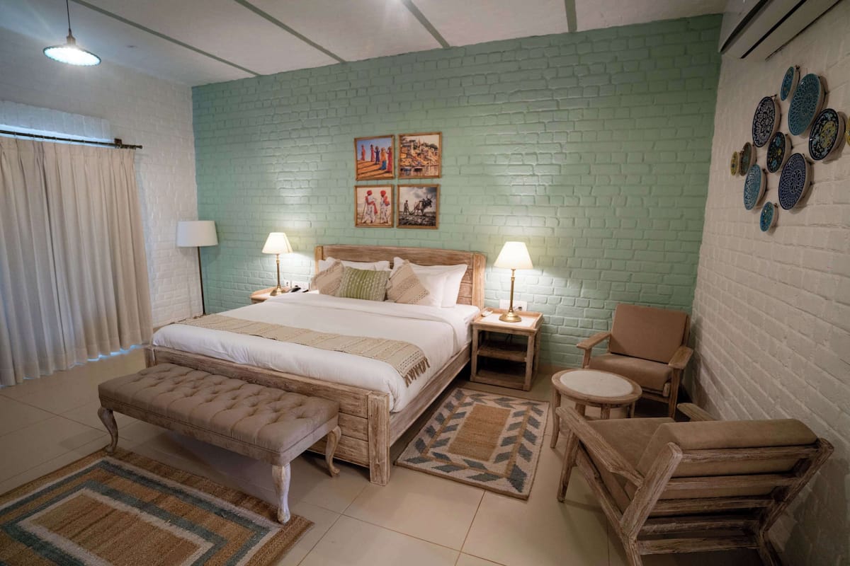 A bedroom with a bed, two bedside tables with lamps, a chair, a bench, and a wall with decorative plates.