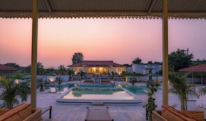A pool area with a house in the background, surrounded by greenery. - Kadamb Bagh (Rajgarh)