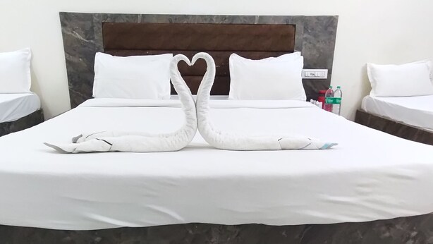 Une chambre d’hôtel avec un grand lit, deux oreillers blancs, une décoration en forme de cœur réalisée avec des serviettes et une tête de lit en marbre.