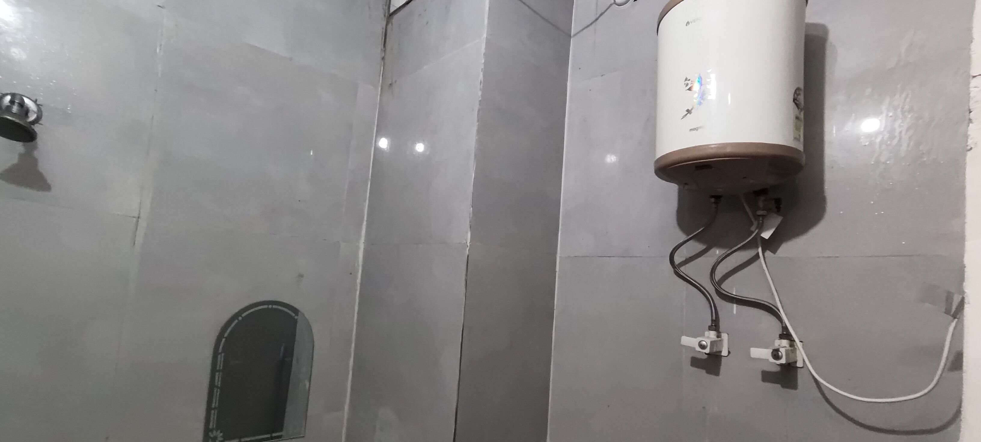A bathroom with a white tiled wall, a showerhead, and a water heater mounted on the wall.