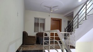 Un couloir doté d’un sol en marbre noir, d’un ventilateur de plafond, d’un canapé marron, d’un meuble gris et d’un escalier avec des rampes en métal.