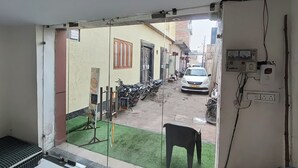 Une vue étroite d’une rue, prise depuis une fenêtre, avec une voiture et des motos garées dans la rue, et une chaise placée à l’extérieur de la fenêtre.