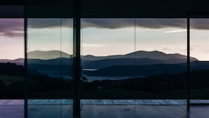 A room with a large window offering a view of a mountainous landscape. - Triptych - The Glass House (Tasman)