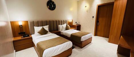 A hotel room with two beds, a wooden headboard, a nightstand with a lamp, a clock on the wall, and a door.