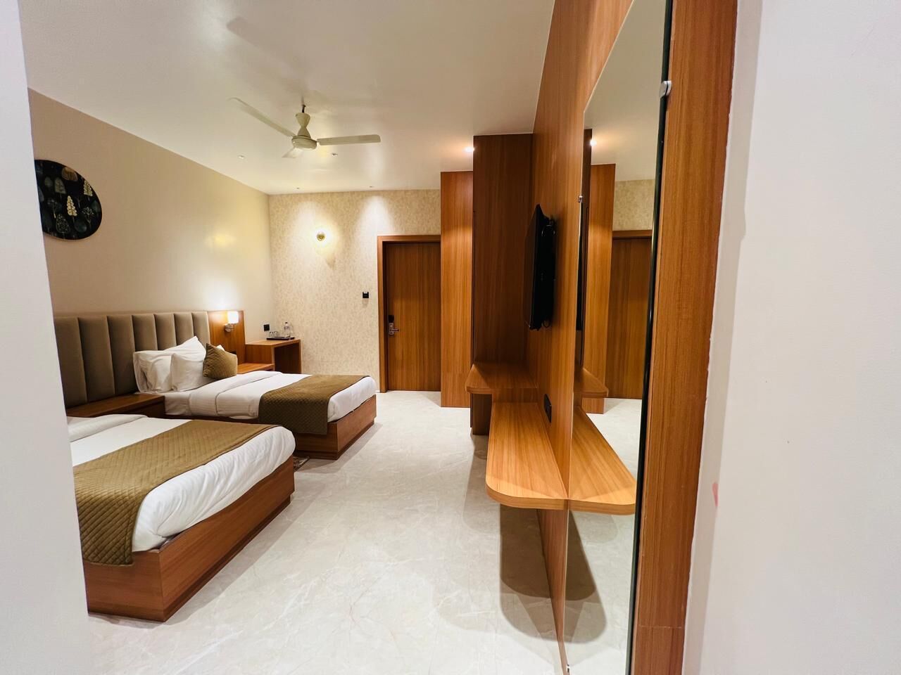 A modern hotel room with two beds, a mirror, a ceiling fan, and a wooden bench.