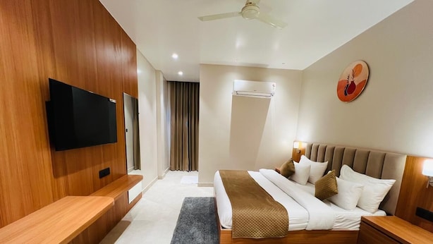 Una camera d'albergo moderna con un letto grande, una testiera in legno, comodini, una TV a schermo piatto montata a parete e una ventola a soffitto.