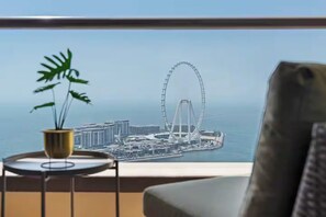 A view from a balcony with a potted plant, a chair, and a large window overlooking a coastal cityscape with a prominent Ferris wheel. - Peaceful Retreat in Downtown (Dubai)