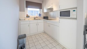A modern kitchen with white cabinets, a built-in microwave, and a window with a view. - Bright apartment with 2 bedrooms and garage (Middelkerke)